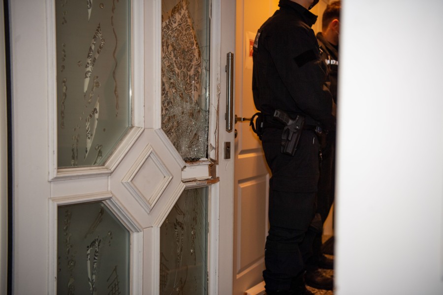 Polizisten stehen neben der zerstörten Tür eines Hauses, das von ihnen durchsucht wurde.