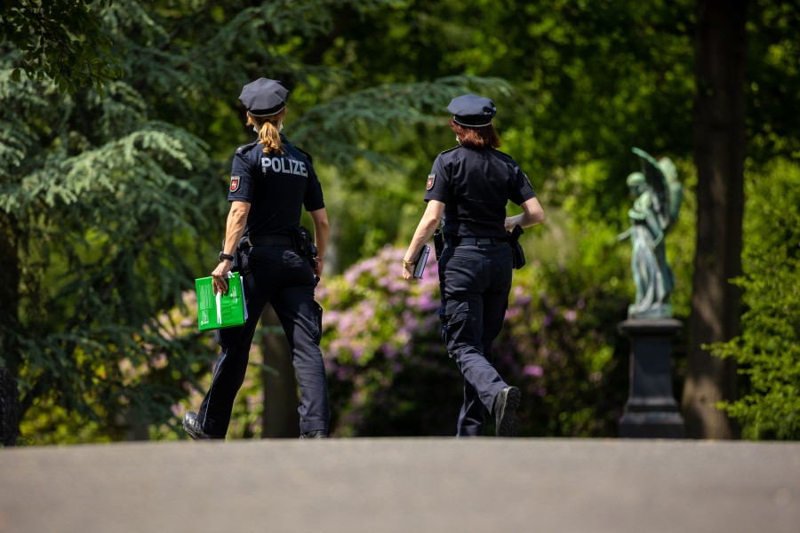 Einsatzkräfte der Polizei gehen vor Beginn der Beerdigung eines Mordopfers über den Stadtfriedhof Stöcken. 