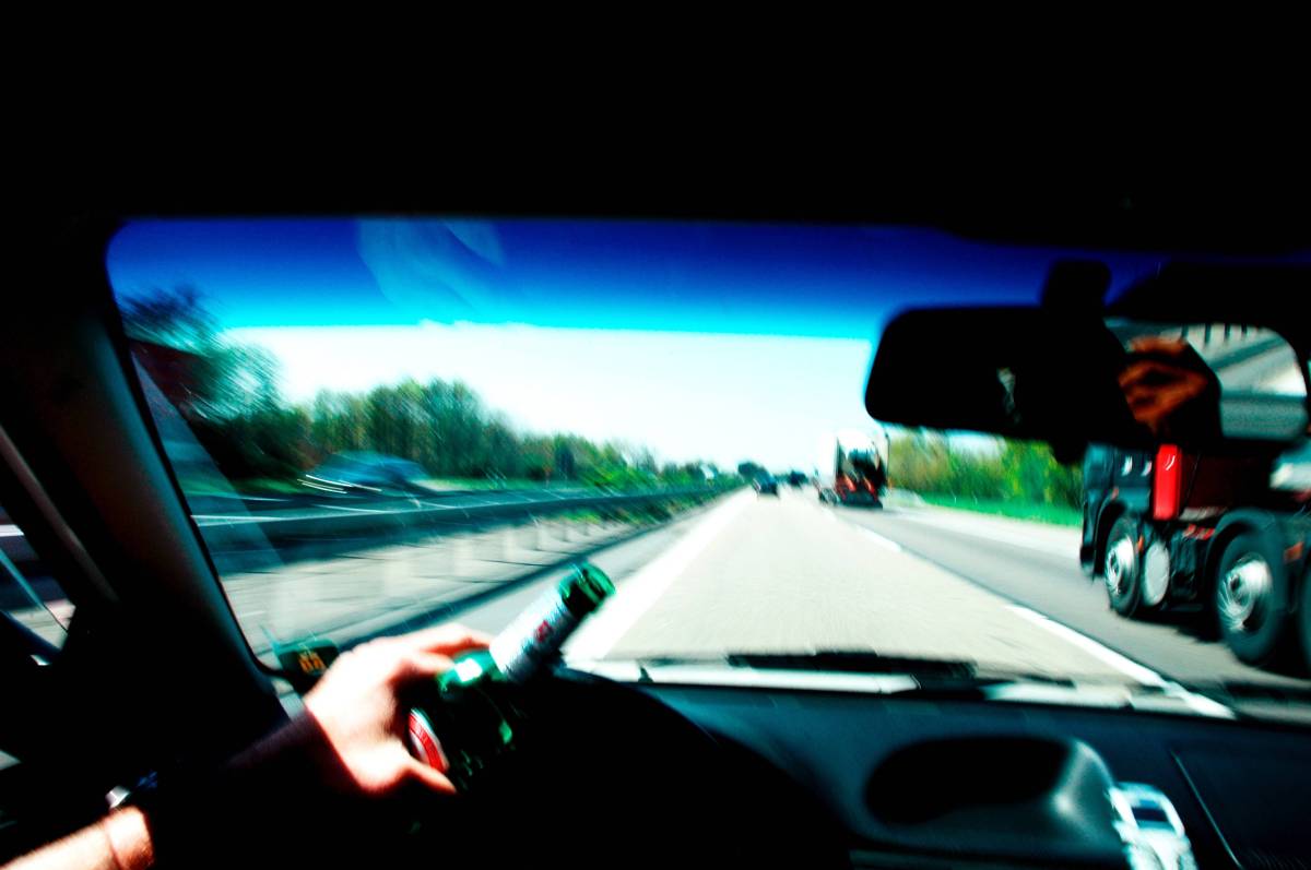 Blick aus Auto auf Autobahn mit Bierflasche am Steuer