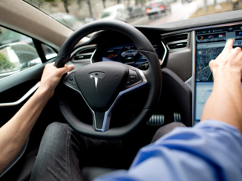 Mann sitzt hinterm Tesla Steuer und zeigt auf Cockpit