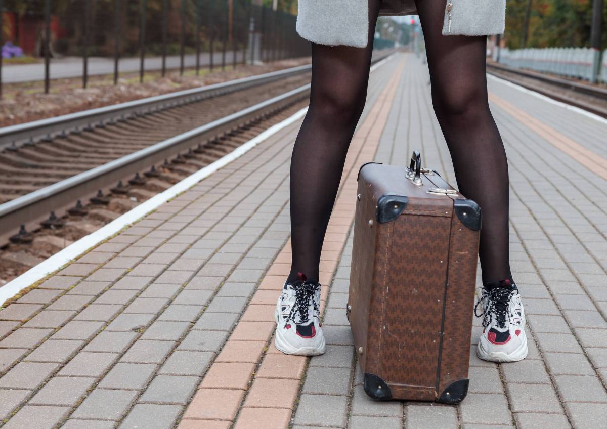 Frau steht mit Koffer am Bahnsteig