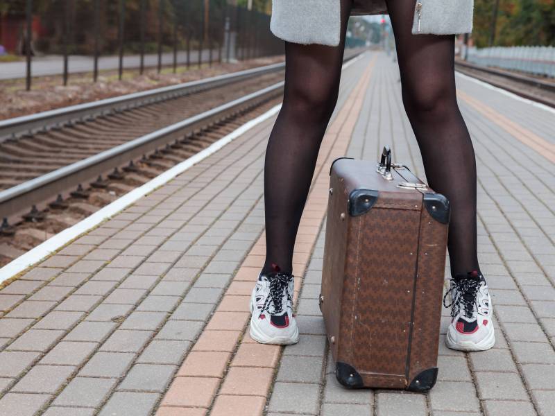 Frau steht mit Koffer am Bahnsteig