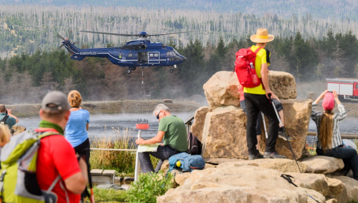 Ein Hubschrauber der Bundespolizei entnimmt Wasser aus einem See am Wurmberg, während zahlreiche Wanderer und Schaulustigen die Löscharbeiten beobachten. Hunderte Einsatzkräfte bekämpften 2022 einen großen Waldbrand im Harz.