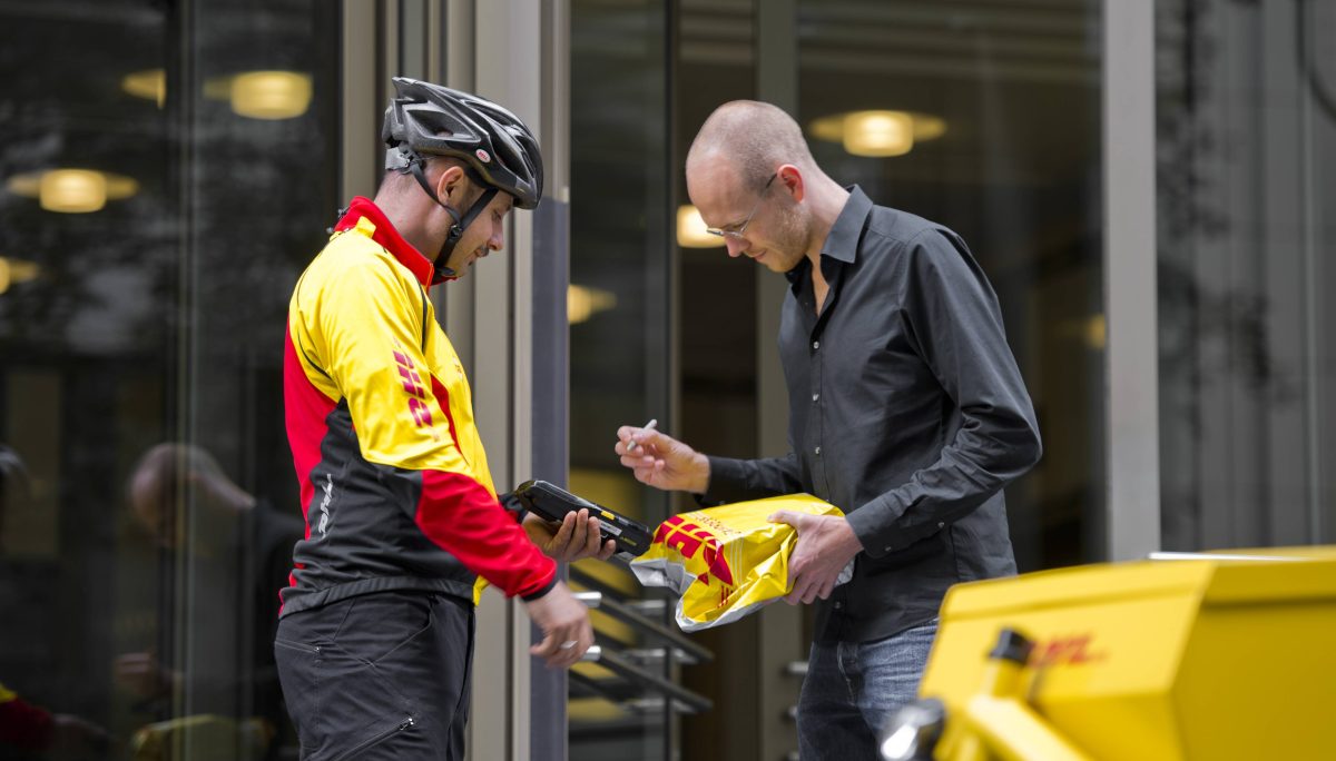 DHL-Fahrradkurier übergibt Kunden ein Paket, der unterschreibt