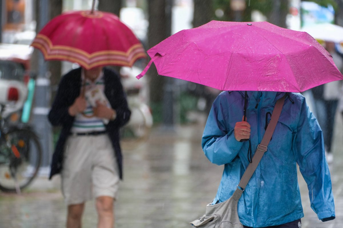 Personen gehen mit Regenschirmen durch den Regen
