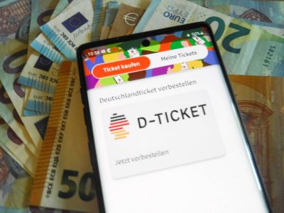 Deutschlandticket auf Handy, das auf Euro-Scheinen liegt