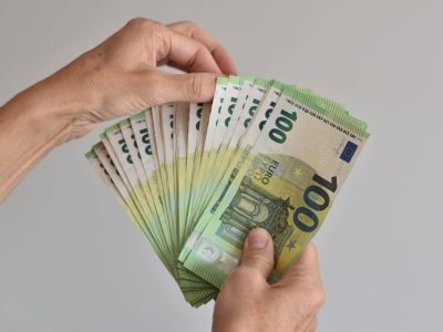 Eine Hand zählt viele einhundert Euro Geldscheine aufgefächert wie bei einem Kartenspiel.