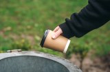 Person schmeißt einen Kaffeebecher in einen Mülleimer im Park