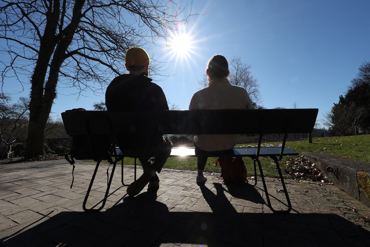 Zwei Menschen sitzen auf einer Parkbank und geniessen genießen die Sonne.