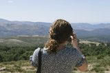 Rückansicht einer jungen Frau, die mit ihrem Mobiltelefon Fotos von der Landschaft macht.